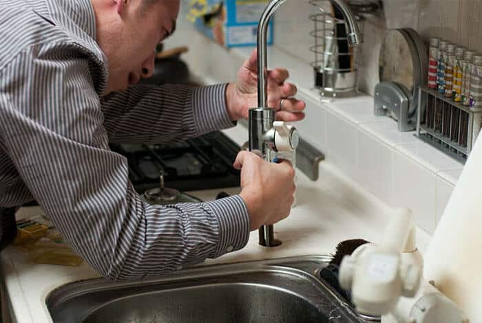 Plumber repairing kitchen faucet in home setting, addressing plumbing issues related to leaks and maintenance.