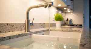 Modern kitchen faucet with running water over a white sink, highlighting potential leaky faucet issues and solutions for homeowners.