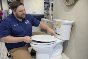 Plumber inspecting a toilet, demonstrating repair techniques, in a showroom setting, highlighting professional plumbing services for toilet issues.